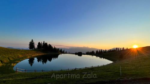 un estanque en un campo con la puesta de sol en el fondo en Apartma Zala, Golte en Mozirska Koča