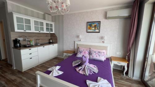 a bedroom with a purple bed and a kitchen at Апартаменти и студия в комплекс Акротирия in Nesebar