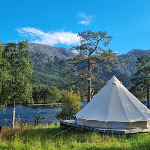 a white tent in the grass next to a lake at Flatheim Glamping in Viksdalen