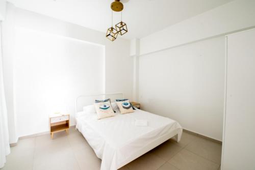 Habitación blanca con cama y lámpara de araña. en Ennea Suites-Light suite, en Flámbouras