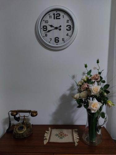 a clock on a wall above a table with a vase of flowers at MILA city center-free parking in Vranje