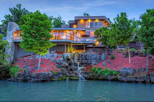 a house on a cliff with a waterfall at Iconic Glass Mansion - Huge Views - Best Location in Osage Beach
