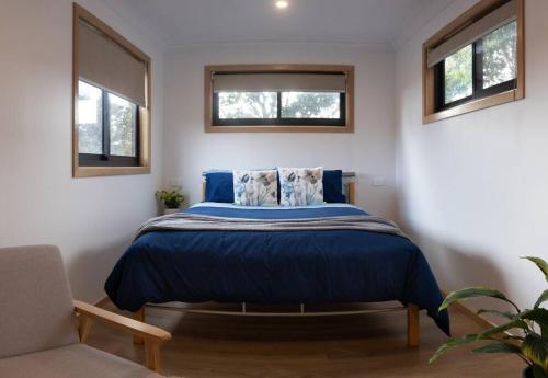 a bedroom with a bed with a blue comforter and two windows at Burnie Unit - The Cape in Burnie