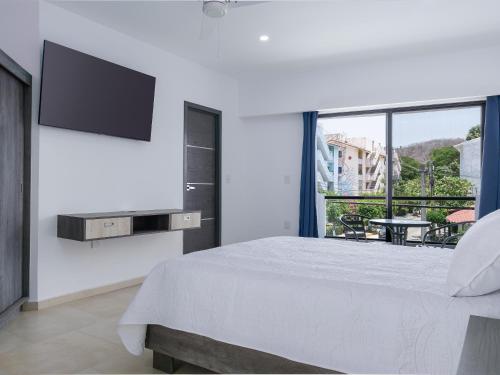- une chambre blanche avec un grand lit et une télévision à écran plat dans l'établissement Casa Xtao Hotel, à Santa Cruz Huatulco