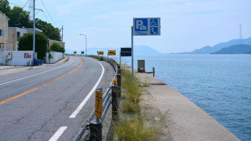 un cartello stradale accanto a una strada vicino all'acqua di Tabist Setouchinoyado Takehara Seaside a Takekara