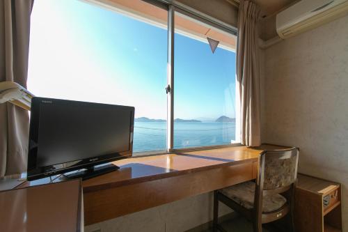 a computer desk with a monitor and a large window at Tabist Setouchinoyado Takehara Seaside in Takekara