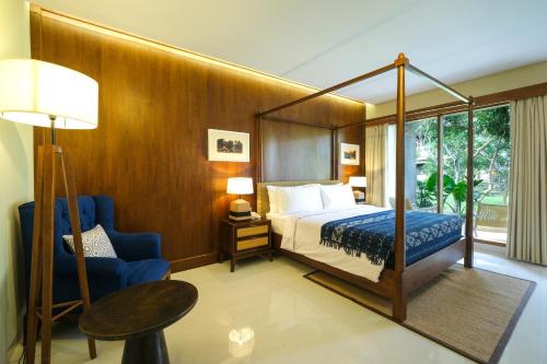 a bedroom with a canopy bed and a blue chair at Bhuwana Ubud Hotel and Farming in Ubud