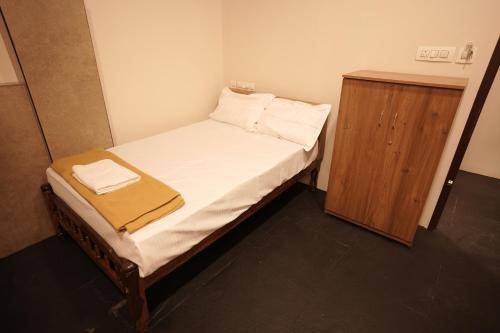 a small bedroom with a bed and a wooden cabinet at Reach Residency in Cochin