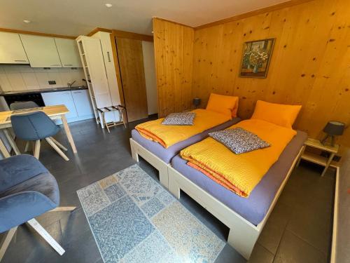 1 Schlafzimmer mit einem Bett mit orangefarbener Bettwäsche und einer Küche in der Unterkunft Alpenchalet Weidhaus Gstaad mit Ferienwohnung-Studio-Stockbettzimmer alle Wohneinheiten separat Buchbar in Gstaad