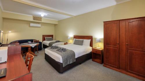 Habitación pequeña con 2 camas y escritorio. en Oasis Motor Inn en Broken Hill