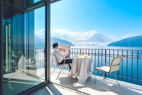 a man sitting at a table on a balcony reading a newspaper at Park Hotel Vitznau in Vitznau