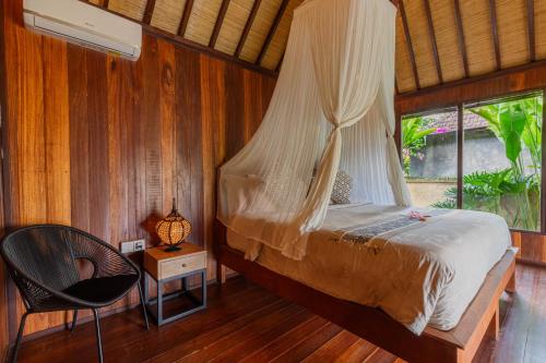 a bedroom with a bed and a chair and a window at NILUH Private Villas Ubud in Ubud