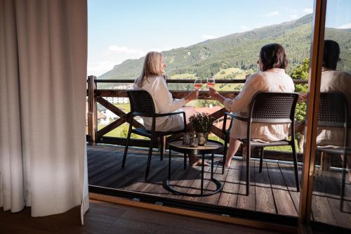 two women sitting at a table on a balcony with wine glasses at Wildkogel Resorts - DAS Bramberg in Bramberg am Wildkogel