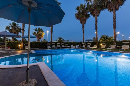 a pool with an umbrella and chairs and palm trees at Kiara Residence in Giulianova