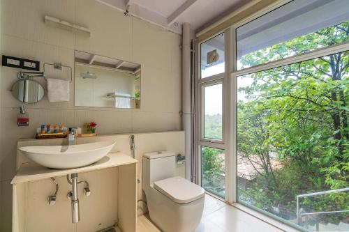 a bathroom with a sink and a toilet and a window at The Glasscape by StayVista - Hillside getaway with Pool and Indoor games in Nashik