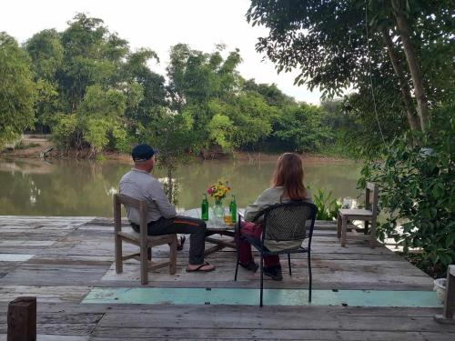a man and woman sitting at a table near a river at สามชุกบ้านสวน in Sam Chuk