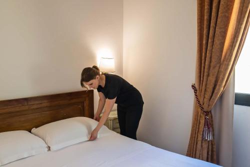 a woman is making a bed in a hotel room at Hotel Machiavelli Palace in Florence