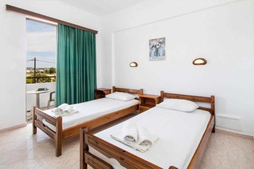 two beds in a room with a large window at Nikos BnB in Faliraki