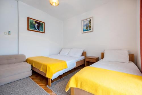 two beds with yellow sheets in a room with a couch at Apartments and rooms Lotus in Neum