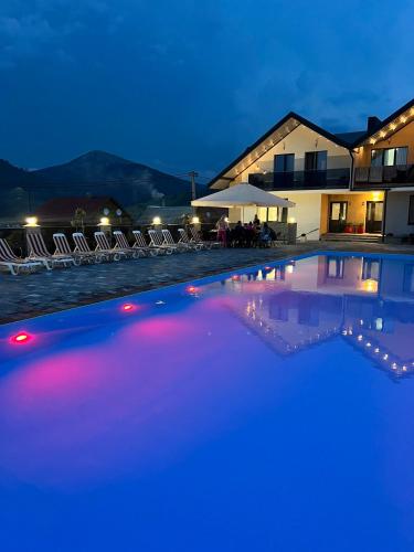 a swimming pool at night with chairs and a building at Guest House Zatyshnyi Dvir in Bukovel