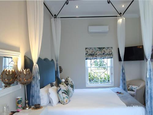 a bedroom with a bed with blue curtains and a window at Fleur du Soleil Luxury Guesthouse in Franschhoek