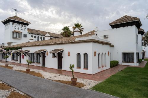 un gran edificio blanco con un patio y palmeras en Hotel El Cortijo Matalascañas, en Matalascañas