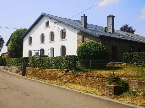 une maison blanche avec un mur en pierre à côté d'une rue dans l'établissement Gîte Les trois charmes, à Gouvy