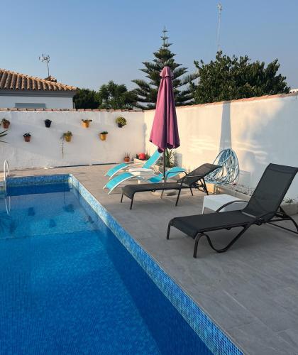 a swimming pool with two lounge chairs and an umbrella at Fantástico chalet con piscina 2 km de la barrosa in Chiclana de la Frontera