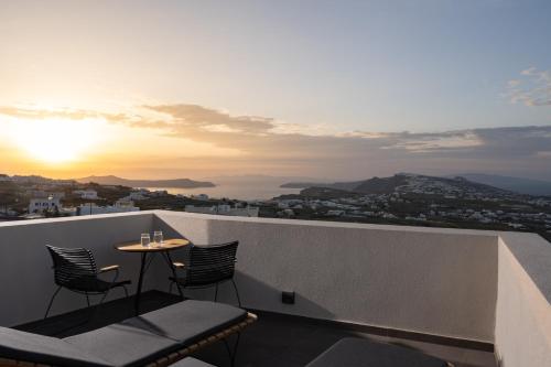 a table and chairs on a balcony with the sunset at Apikia Santorini in Pirgos