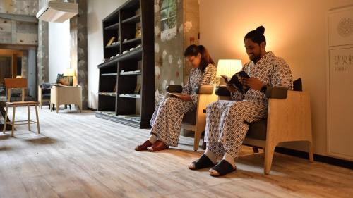 a man and a woman sitting in chairs with their phones at Shin Toji Hotel Lulud in Nakanojo