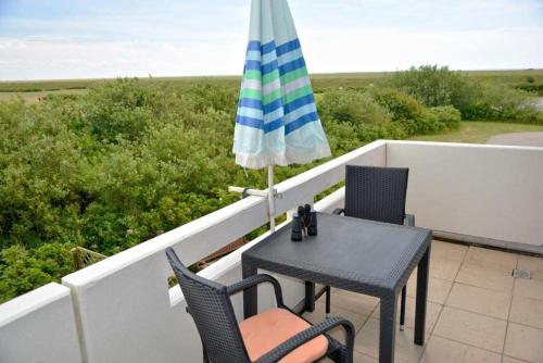 a table and chairs on a balcony with an umbrella at Haus am Golfplatz Nr 06 Ferienwohnung Strandblick in Süderhöft