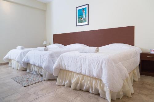 two beds in a room with white comforters on them at Hosteria Palmetto in Playas