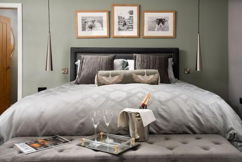uma cama com um edredão cinzento e uma mesa com copos de vinho em Roundhill Coach House 