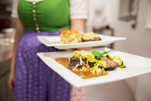 a woman is holding two plates of food at Hotel Annelies in Ramsau am Dachstein