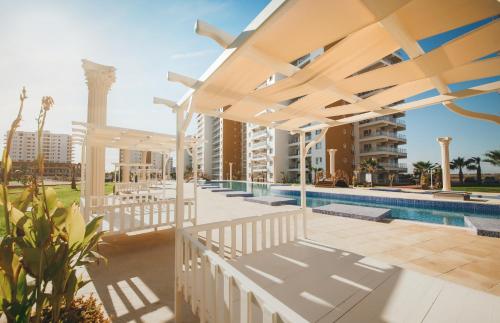 a patio with a pool and a white pergola at Amadeus Holiday Apartments in Caesar Resort & SPA, Long Beach in Perivolia tou Trikomou