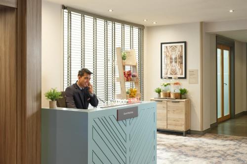 a man talking on a cell phone at a reception desk at Leonardo Royal Hotel Oxford in Oxford