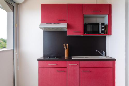 a red kitchen with a sink and a microwave at Hôtel Iloma in Sainte-Luce