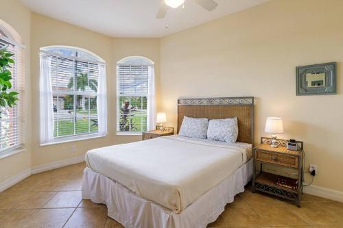 een slaapkamer met een bed met 2 nachtkastjes en 2 ramen bij Villa Maxos - Boaters dream 4br/3 bath pool / spa in Cape Coral