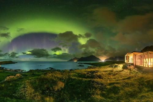 una vista de la aurora con una casa en un campo en where the ocean meets land, en Ramberg