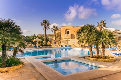 uma grande piscina com palmeiras em frente a um edifício em Villagg tal-Fanal em Għasri