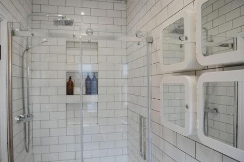 a white tiled bathroom with a shower and two mirrors at The Snug in Riccall