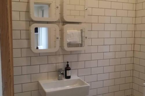 a white tiled bathroom with a sink and two mirrors at The Snug in Riccall