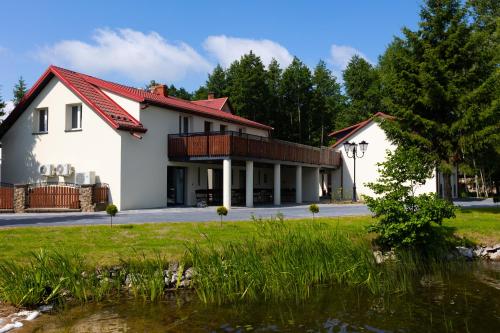 une maison blanche avec un toit rouge et un étang dans l'établissement Agroturystyka Kalinka, à Wiżajny
