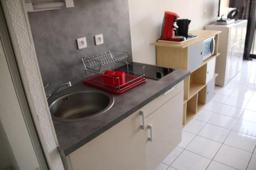 - une cuisine avec un évier et un plateau rouge sur le comptoir dans l'établissement Studio 216, Port Vénus au village naturiste, au Cap d'Agde