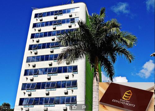 a tall white building with a palm tree in front of it at Hotel Estação Norte - Fácil acesso ao Imbel e o distrito industrial e colégio Militar - By Up Hotel in Juiz de Fora