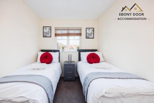 2 camas en una habitación con 2 almohadas rojas en Ebony Door Accommodation Charming 3 Bedroom House Thurrock Sleeps 6, en Grays