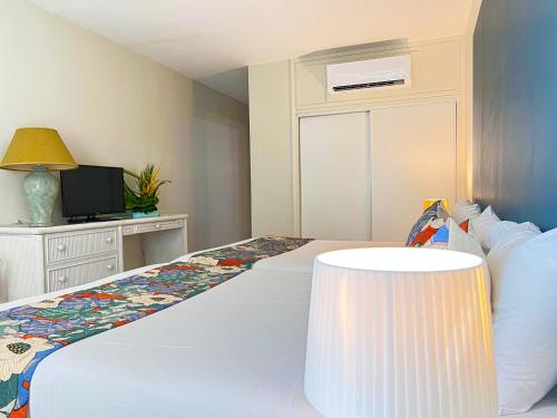 a bedroom with a white bed with a lamp and a tv at Karibea Squash Hôtel in Fort-de-France