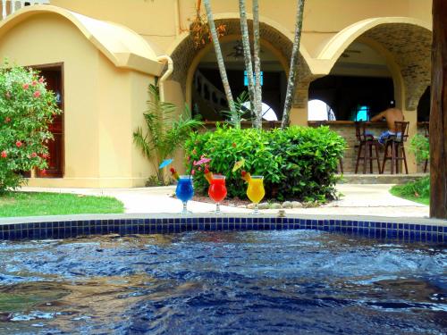 three colorful cocktails sitting on the side of a swimming pool at Hotel Delfin Playa Bejuco in Esterillos Este