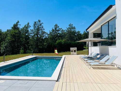 a swimming pool with chairs and an umbrella next to a house at Vila Prisunca jacuzzi & swimming pool in Pazin