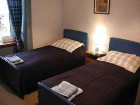 Dunroamin Hotel في Bonar Bridge: غرفة نوم بسريرين وطاولة بها مصباح